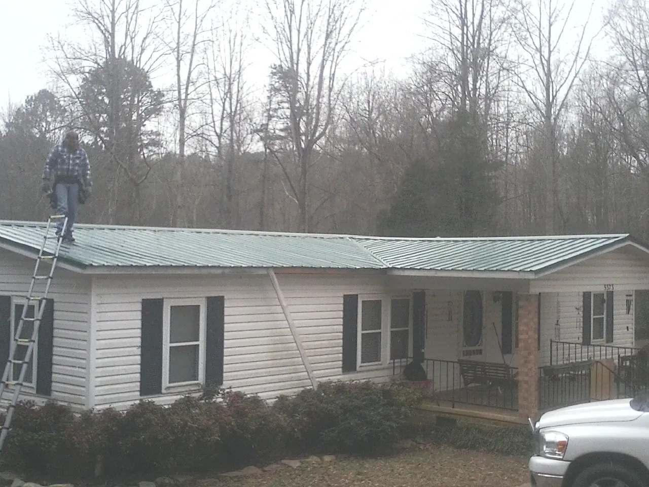 Worker on a ladder beside a new green metal roof on a ranch home in Wabash