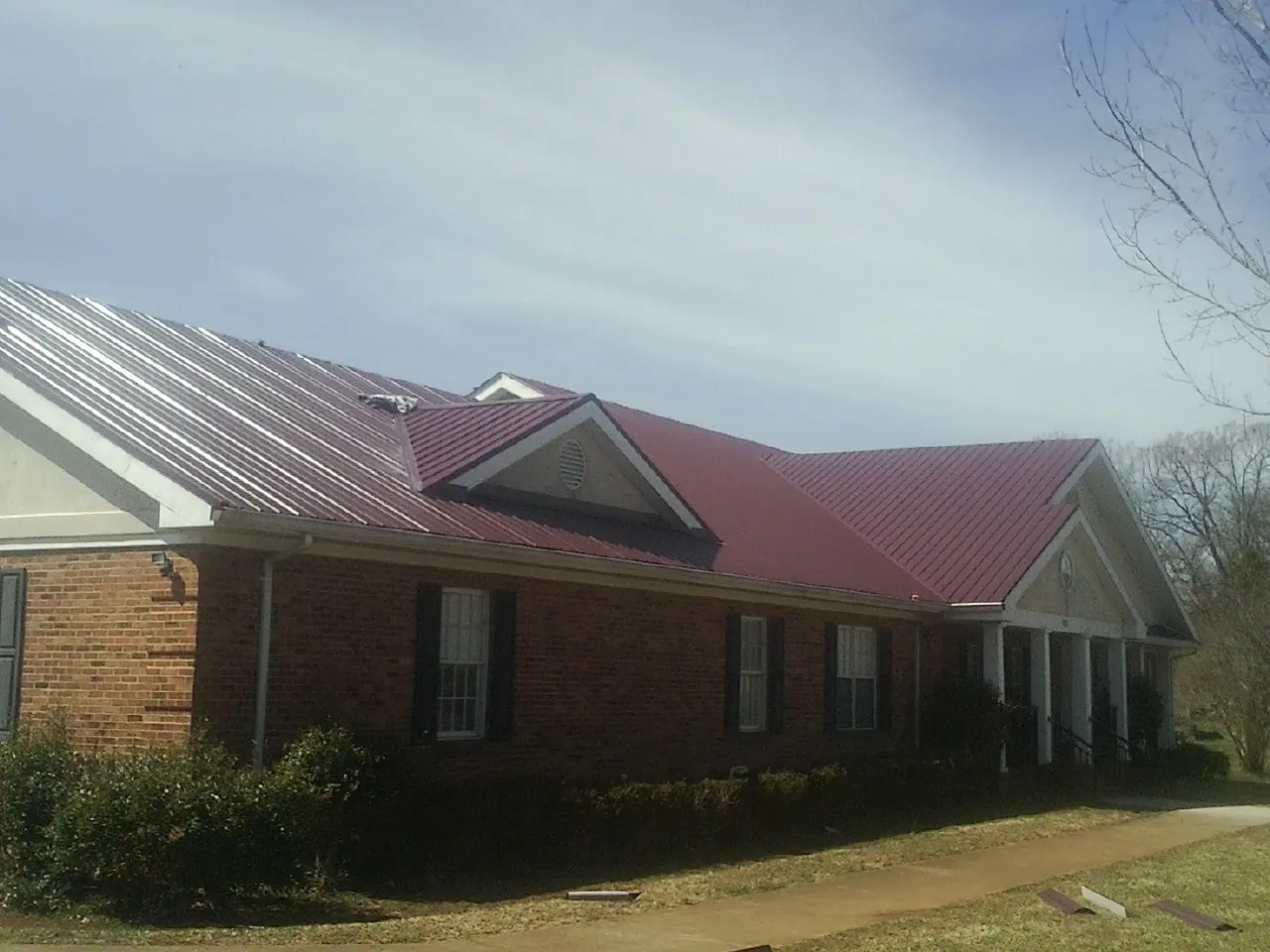 Red metal roof with gabled entries on a long brick building, from a Hail Damage Roof Repair job in Wabash
