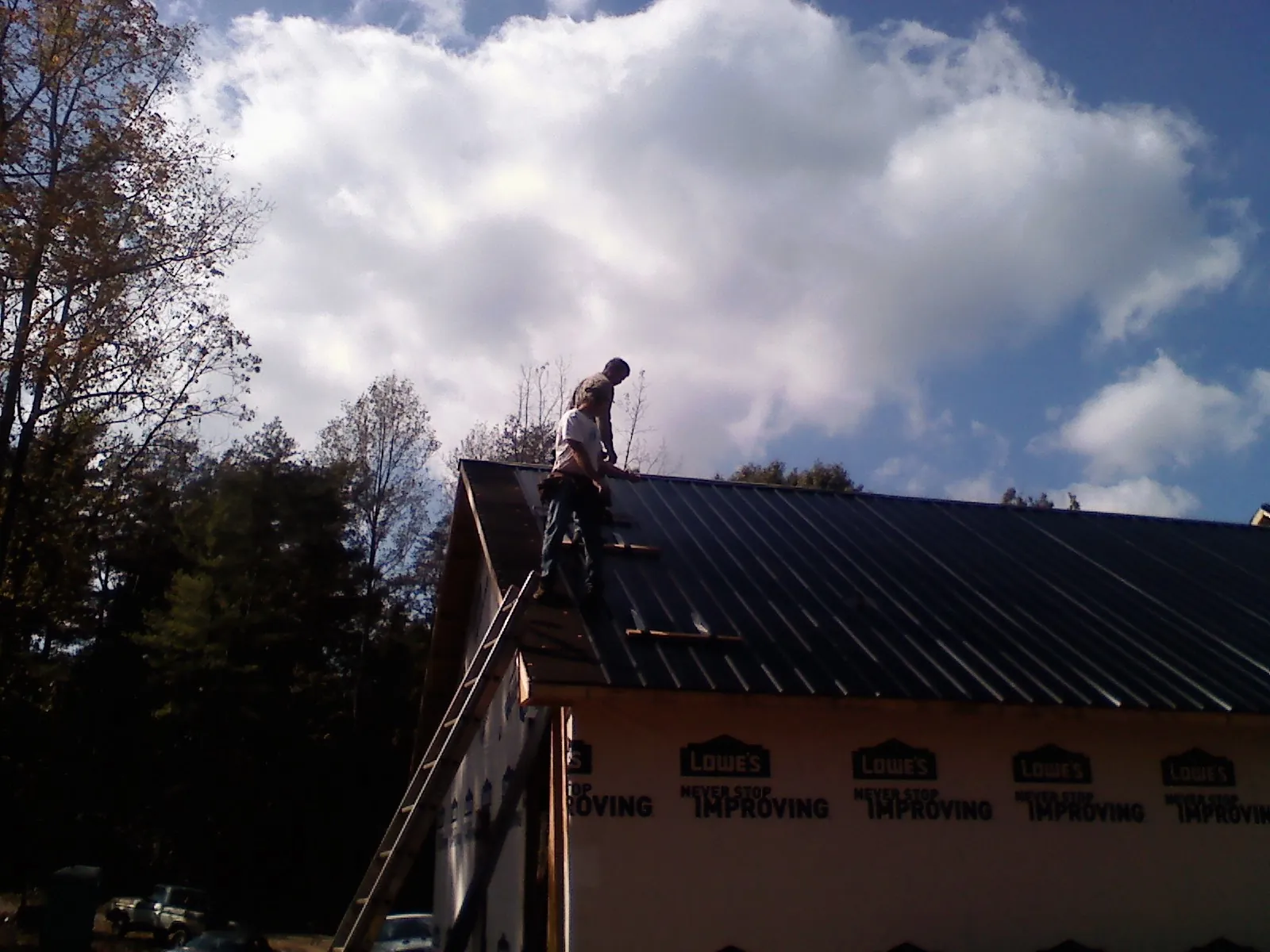 Roofer fastening dark metal panels high against a cloudy sky, from a Roof Inspection job in Wabash