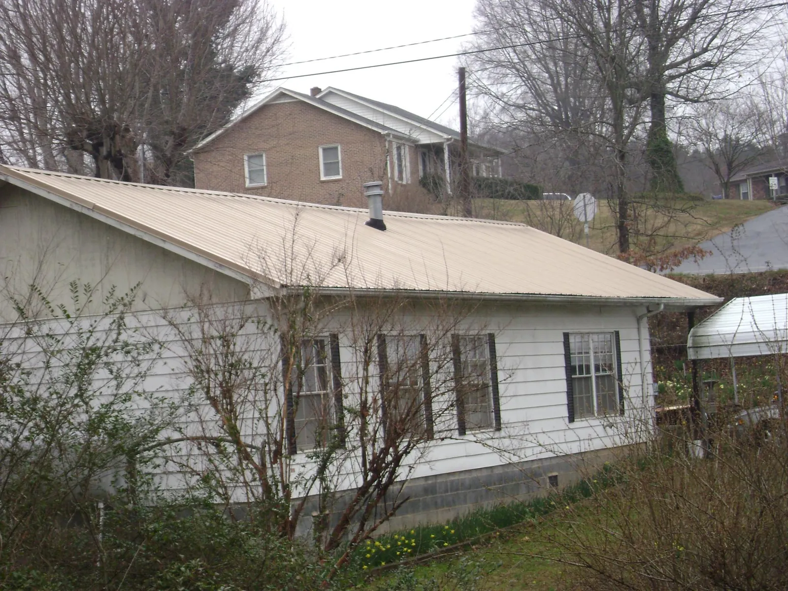 Tan metal roof on a white sided house set into a hillside — Commercial Roofing by Roofing Brothers in Wabash